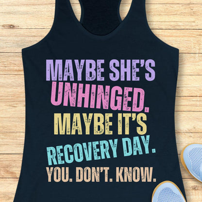 A navy racerback tank top with a colorful distressed text graphic reading 'MAYBE SHE'S UNHINGED. MAYBE IT'S RECOVERY DAY.