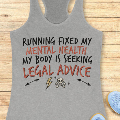 A heather gray racerback tank top laid flat on a light wood plank background, featuring a graphic print with the text 'RUNNING FIXED MY MENTAL HEALTH MY BODY IS SEEKING LEGAL ADVICE' in black and rust-red lettering, along with small black arrow, lightning bolt, skull, and crossbones illustrations.