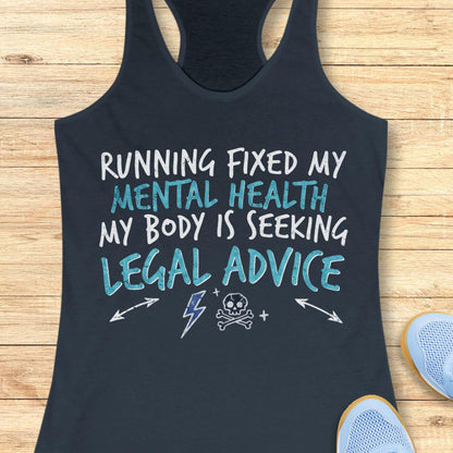 A indigo racerback tank top laid flat on a light wood surface, featuring the text 'RUNNING FIXED MY MENTAL HEALTH MY BODY IS SEEKING LEGAL ADVICE' in white and light blue lettering, with small white graphic icons below. Partial blue sneakers are visible at the bottom right as styling props.