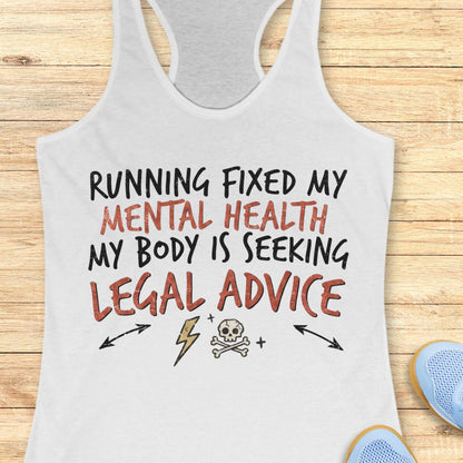 A white racerback tank top with a humorous graphic print reading 'RUNNING FIXED MY MENTAL HEALTH MY BODY IS SEEKING LEGAL ADVICE' in black and reddish-brown lettering, displayed flat on a light wood background with partial blue sneakers visible at the bottom right.