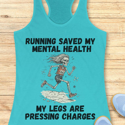 A turquoise racerback tank top laid flat on a light wood surface, featuring a black graphic of a running skeleton and the text 'RUNNING SAVED MY MENTAL HEALTH' and 'MY LEGS ARE PRESSING CHARGES'. A partial blue shoe is visible at the bottom right.