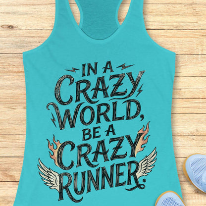 A turquoise racerback tank top laid flat on a light wood surface, featuring the phrase 'IN A CRAZY WORLD, BE A CRAZY RUNNER' in large black lettering with flame and wing graphics. Part of a light blue shoe is visible at the bottom right.
