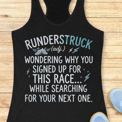 A black racerback tank top laid flat on a light wood surface, featuring a humorous white and light blue graphic that reads 'RUNDERSTRUCK (adj.) WONDERING WHY YOU SIGNED UP FOR THIS RACE.