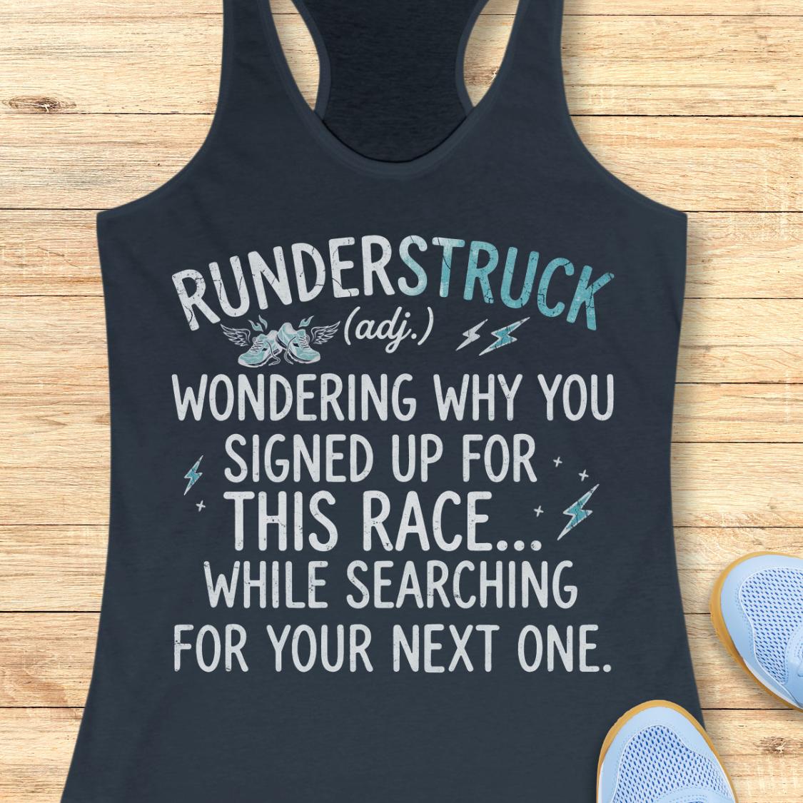 A indigo racerback tank top laid flat on a light wood background, printed with the phrase 'RUNDERSTRUCK (adj.) WONDERING WHY YOU SIGNED UP FOR THIS RACE.