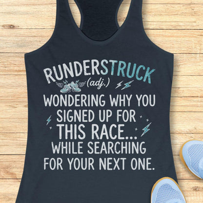 A indigo racerback tank top laid flat on a light wood background, printed with the phrase 'RUNDERSTRUCK (adj.) WONDERING WHY YOU SIGNED UP FOR THIS RACE.