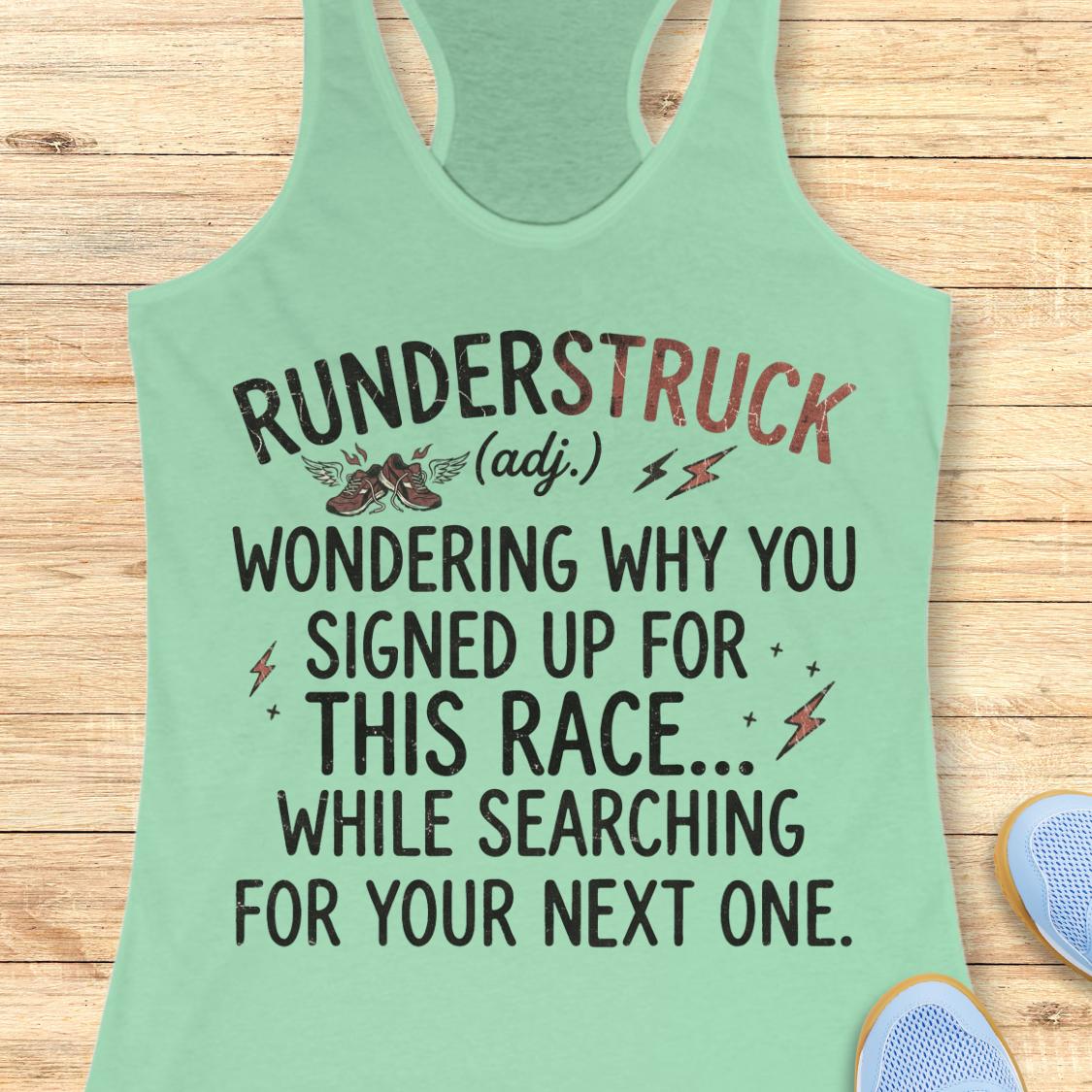A mint green racerback tank top laid flat on a light wood background, featuring a humorous race-themed graphic that reads 'RUNDERSTRUCK (adj.) WONDERING WHY YOU SIGNED UP FOR THIS RACE.