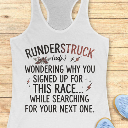 A white racerback tank top with a humorous graphic print on a light wood background, styled with blue sneakers partially visible in the corners.