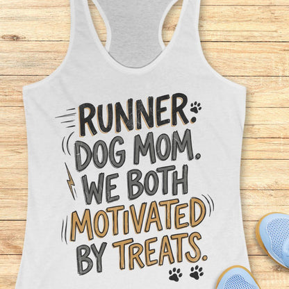 A white racerback tank top laid flat on a light wood background, featuring the printed phrase 'RUNNER DOG MOM WE BOTH MOTIVATED BY TREATS' in black and tan lettering with small paw print and lightning bolt accents. Part of a blue shoe is visible at the bottom right as a styling prop.