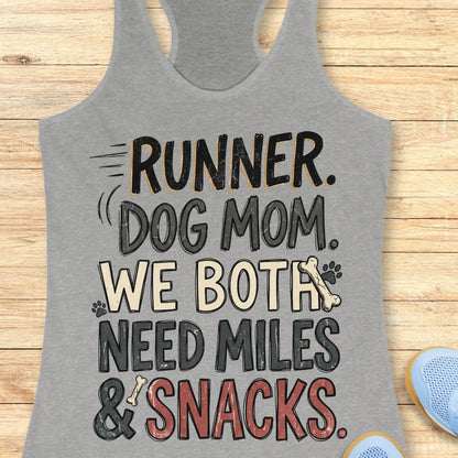 A heather gray racerback tank top laid flat on a light wood background, featuring the text 'RUNNER. DOG MOM.