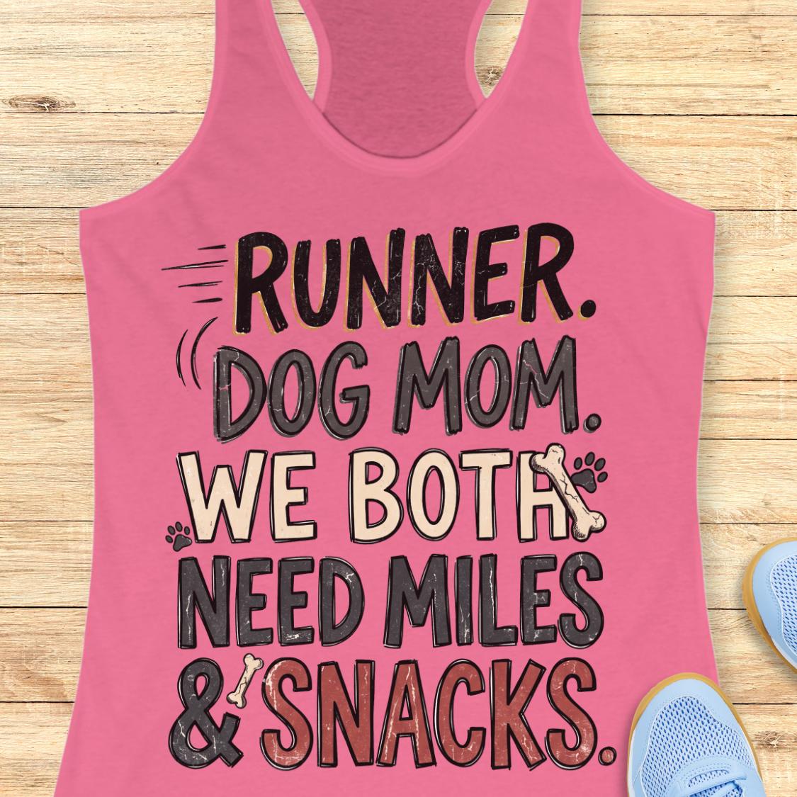 A pink racerback tank top laid flat on a light wood surface, featuring the text 'RUNNER. DOG MOM.
