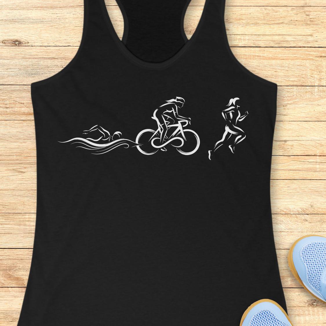 A black racerback tank top laid flat on a light wood background, featuring a white graphic print of a triathlon sequence with a swimmer, cyclist, and runner. Partial blue sneakers are visible at the bottom right corner.