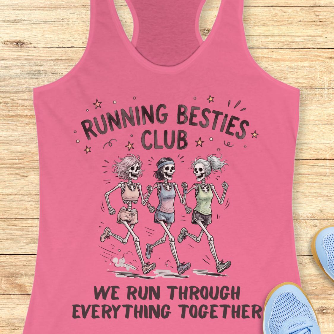 A pink racerback tank top laid flat on a light wood surface, featuring a graphic of three running skeletons with the text 'RUNNING BESTIES CLUB' and 'WE RUN THROUGH EVERYTHING TOGETHER.' Partial blue shoes are visible at the edges as styling props.