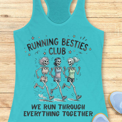 A turquoise racerback tank top laid flat on a light wood surface, featuring a printed graphic of three running skeletons with the text 'RUNNING BESTIES CLUB' and 'WE RUN THROUGH EVERYTHING TOGETHER.' A partial blue shoe is visible at the lower right edge.