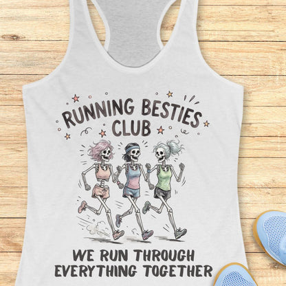 A white racerback tank top laid flat on a light wood background, featuring a printed graphic of three running skeletons with the text 'RUNNING BESTIES CLUB' and 'WE RUN THROUGH EVERYTHING TOGETHER.' A blue shoe is partially visible at the lower right as a styling prop.