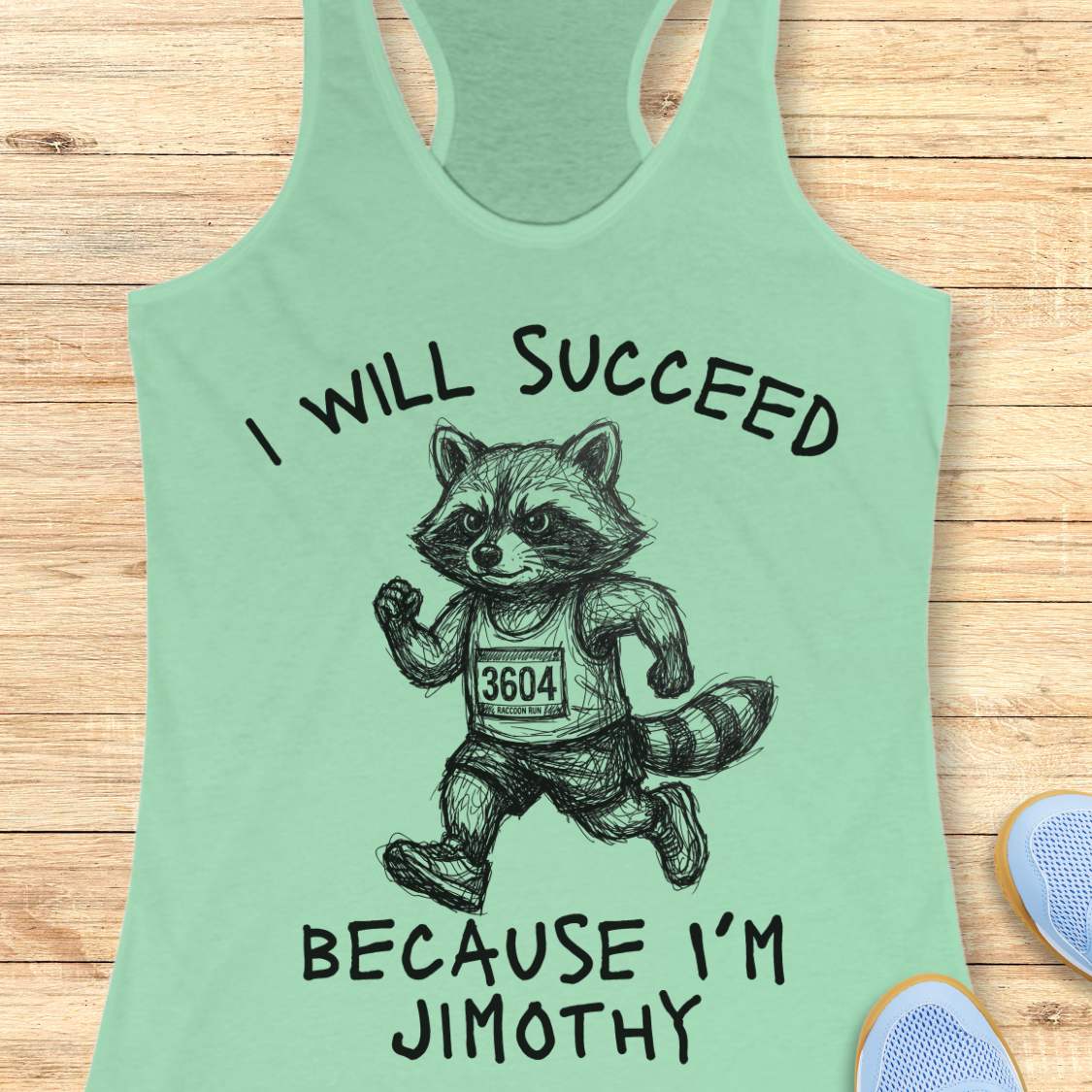 A mint green racerback tank top laid flat on a light wood background, featuring a black graphic of a raccoon running with the text 'I WILL SUCCEED BECAUSE I'M JIMOTHY'.