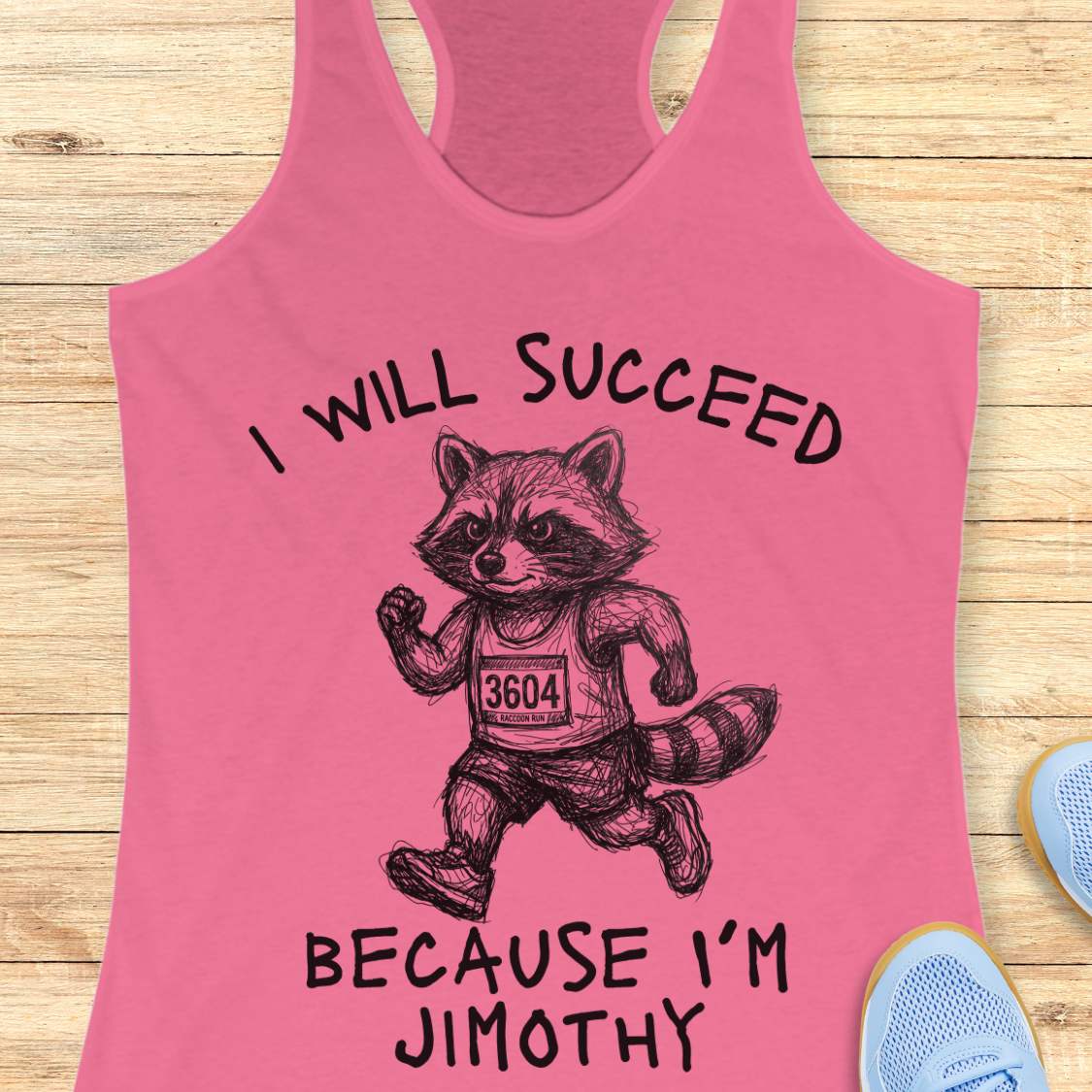A pink racerback tank top laid flat on a light wood surface, featuring a black line-art raccoon running with the text 'I WILL SUCCEED BECAUSE I'M JIMOTHY'. Partial blue shoes are visible at the edges as styling props.