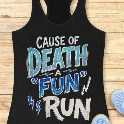 A black racerback tank top laid flat on a light wood background, featuring a distressed graphic that reads 'CAUSE OF DEATH A "FUN" RUN' in white and blue lettering. Part of a light blue shoe is visible at the bottom right as a styling prop.