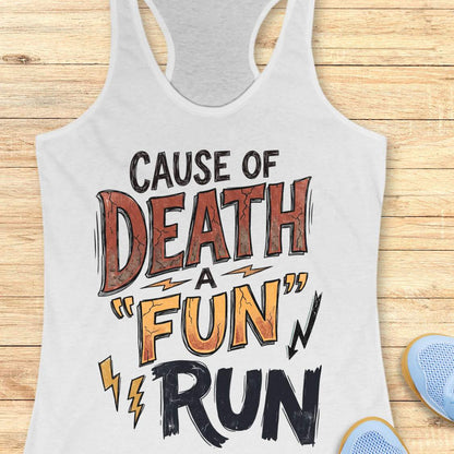A white racerback tank top with a bold graphic print reading 'CAUSE OF DEATH A "FUN" RUN' in black, orange, and brown lettering, laid flat on a light wood plank background with partial blue sneakers visible at the edges.