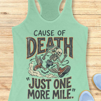 A mint green racerback tank top laid flat on a light wood background, featuring a graphic of a skeleton running with a boot and the text 'CAUSE OF DEATH "JUST ONE MORE MILE"'.