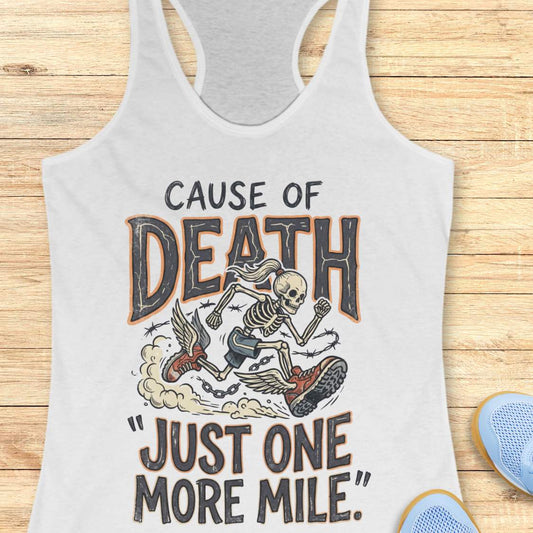 A white racerback tank top laid flat on a light wood background, featuring a graphic print of a skeleton running with a chain and the text 'CAUSE OF DEATH "JUST ONE MORE MILE"'. Partial blue shoes are visible at the bottom right as styling props.