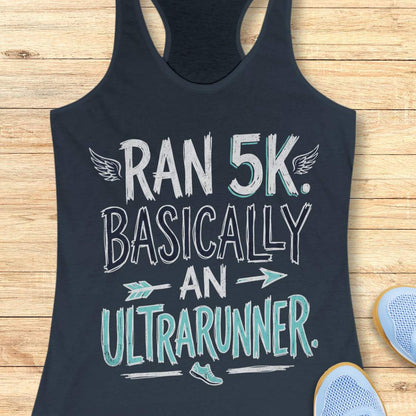 A indigo racerback tank top laid flat on a light wood background, printed with the phrase 'RAN 5K. BASICALLY AN ULTRARUNNER.