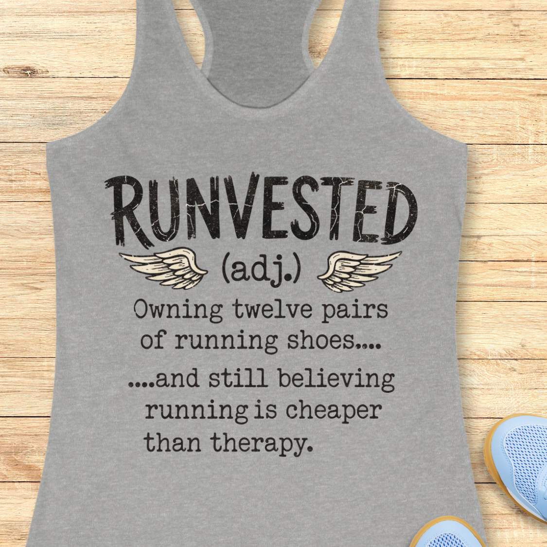 A heather gray racerback tank top with black printed text reading 'RUNVESTED (adj.) Owning twelve pairs of running shoes.