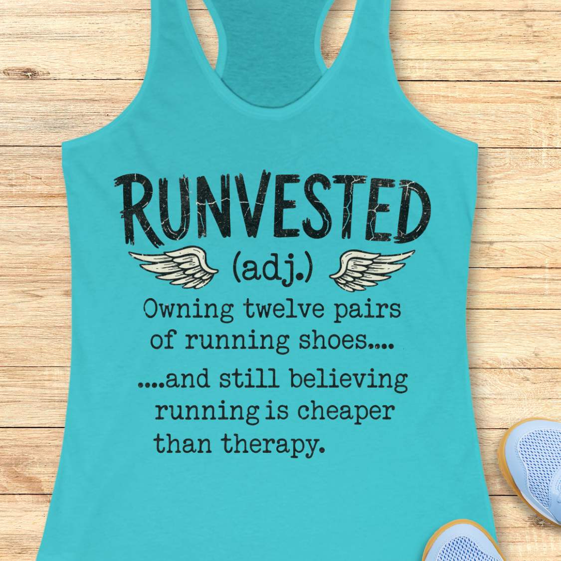 A turquoise racerback tank top laid flat on a light wood surface, printed with the word 'RUNVESTED' and a humorous running-related definition in black text with small wing graphics.