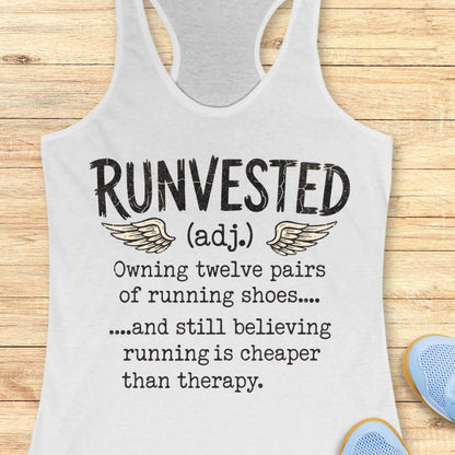 A white racerback tank top laid flat on a light wood background, printed with the word 'RUNVESTED' and a humorous running-themed definition. Partial blue shoes appear at the bottom right as styling props.