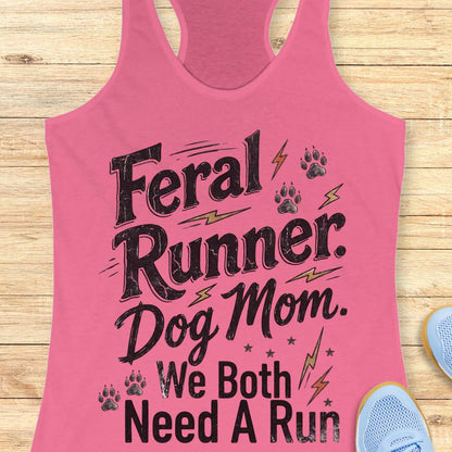 A pink racerback tank top laid flat on a light wood surface, featuring the text 'Feral Runner. Dog Mom.
