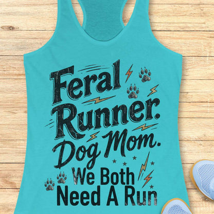 A turquoise racerback tank top laid flat on a light wood surface, printed with the phrase 'Feral Runner. Dog Mom.