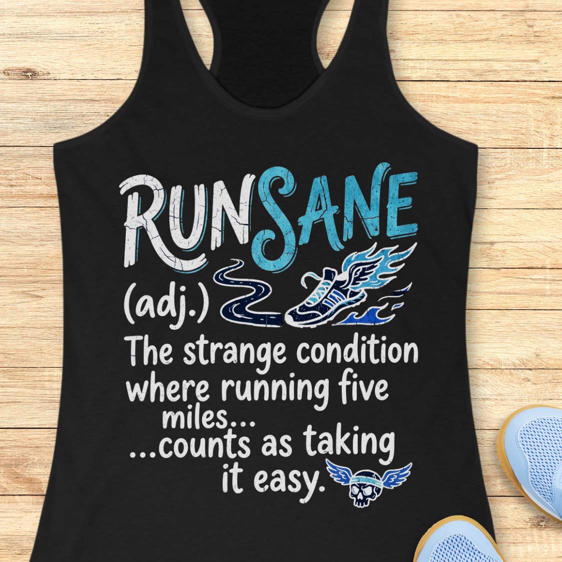 A black racerback tank top laid flat on a light wood background, featuring a white and blue graphic that reads 'RUNSANE (adj.) The strange condition where running five miles.