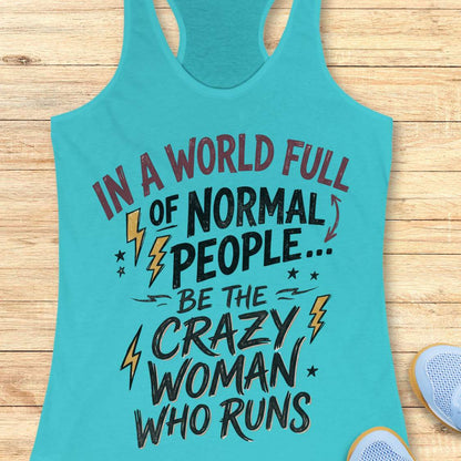A turquoise racerback tank top laid flat on a light wood surface, featuring a motivational graphic that reads 'IN A WORLD FULL OF NORMAL PEOPLE.