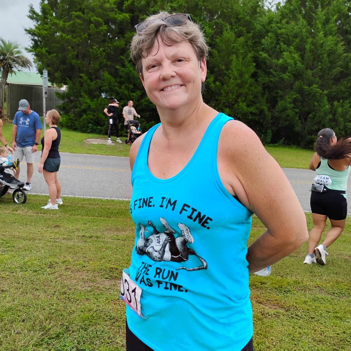 A runner woman wearing a blue tank top with an image of a runner possum playing dead, and th etext - It's fine. I'm fine. The run was fine. 