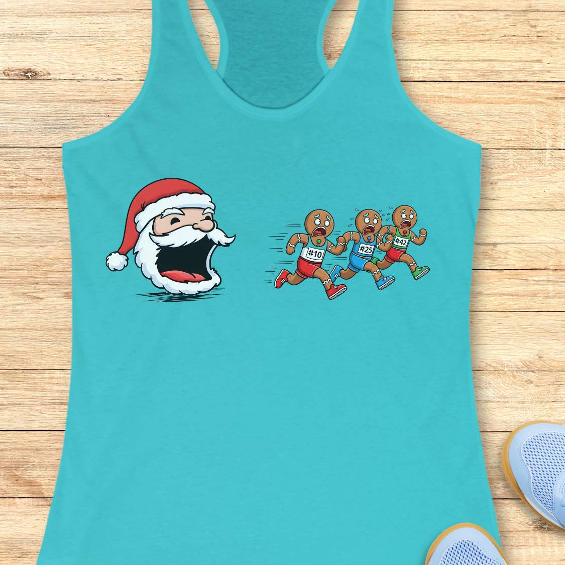 A turquoise racerback tank top laid flat on a light wood surface, featuring a cartoon graphic of a Santa Claus head with an open mouth facing three cartoon runners wearing bib numbers 101, 102, and 103.