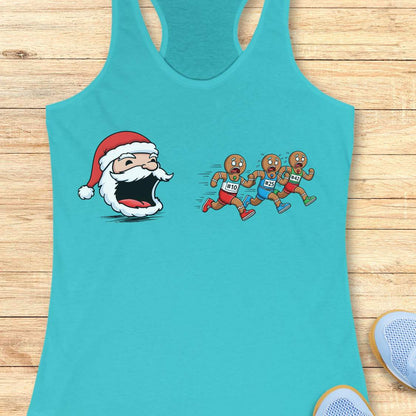 A turquoise racerback tank top laid flat on a light wood surface, featuring a cartoon graphic of a Santa Claus head with an open mouth facing three cartoon runners wearing bib numbers 101, 102, and 103.