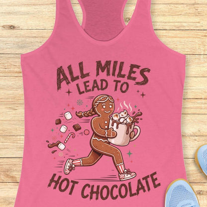 pink running tank top featuring a cartoon gingerbread runner carrying a steaming mug of hot chocolate topped with marshmallows. Chocolate pieces, marshmallows, candy canes, and winter-themed accents surround the character. The design includes the phrase 'ALL MILES LEAD TO HOT CHOCOLATE.