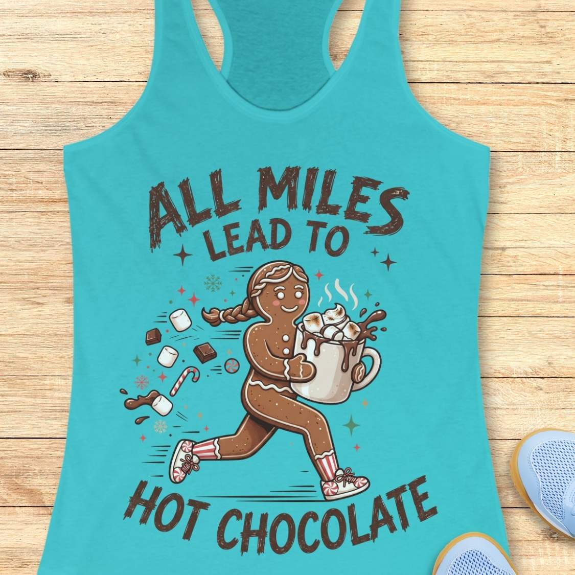 blue running tank top featuring a cartoon gingerbread runner carrying a steaming mug of hot chocolate topped with marshmallows. Chocolate pieces, marshmallows, candy canes, and winter-themed accents surround the character. The design includes the phrase 'ALL MILES LEAD TO HOT CHOCOLATE.