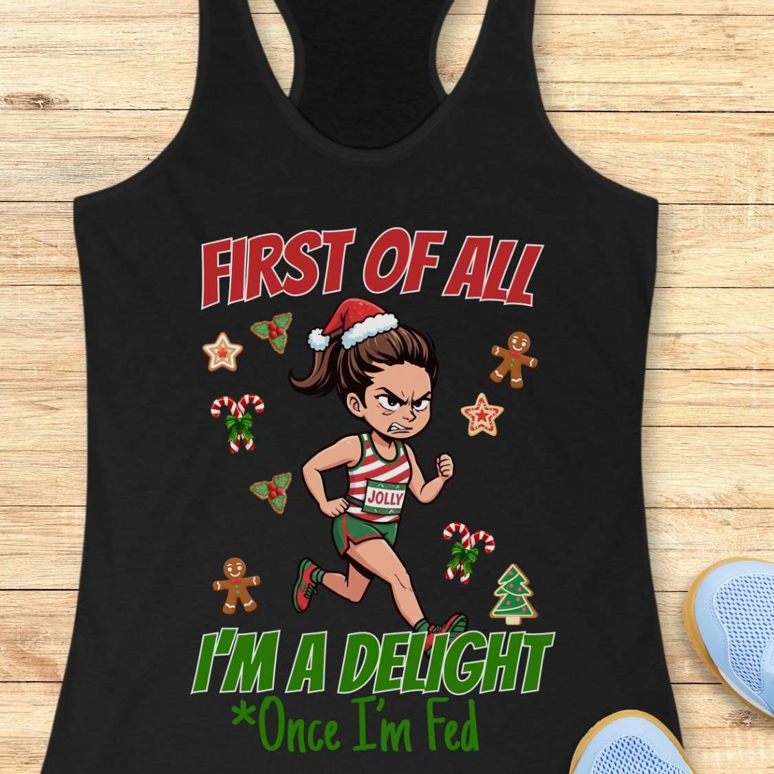 black women's racerback tank top featuring a cartoon holiday runner in a striped red, green, and white running outfit with a Santa hat. The runner is surrounded by festive Christmas elements including candy canes, gingerbread cookies, holly, star cookies, and a Christmas tree. The design reads: “FIRST OF ALL” above the runner and “I’M A DELIGHT Once I’m Fed” below. The artwork combines holiday humor with running culture in a playful, festive style.