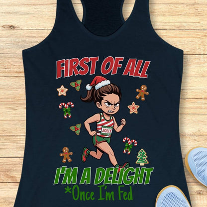 navy women's racerback tank top featuring a cartoon holiday runner in a striped red, green, and white running outfit with a Santa hat. The runner is surrounded by festive Christmas elements including candy canes, gingerbread cookies, holly, star cookies, and a Christmas tree. The design reads: “FIRST OF ALL” above the runner and “I’M A DELIGHT Once I’m Fed” below. The artwork combines holiday humor with running culture in a playful, festive style.