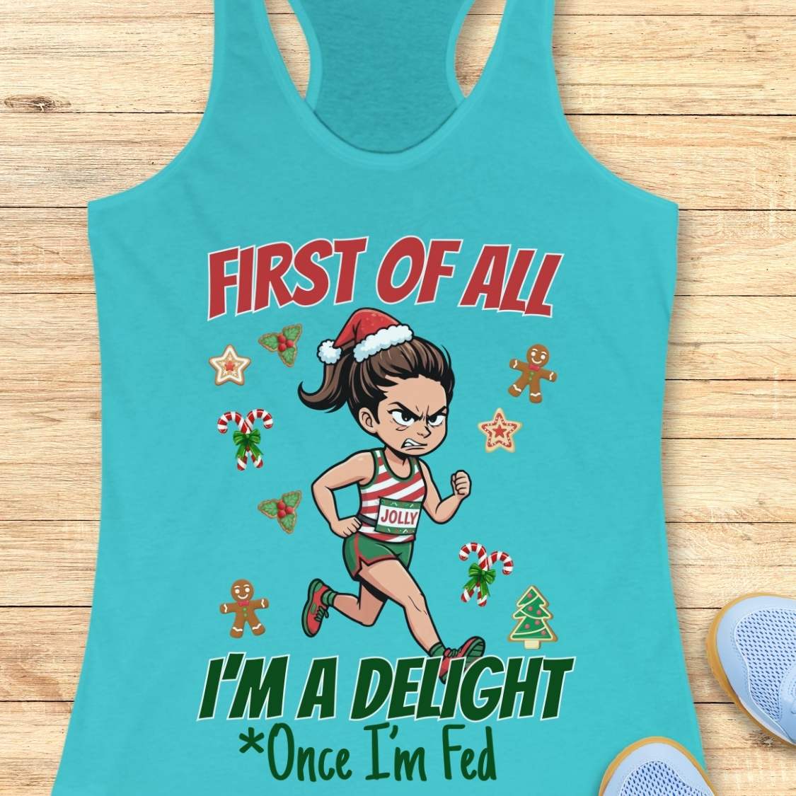 blue women's racerback tank top featuring a cartoon holiday runner in a striped red, green, and white running outfit with a Santa hat. The runner is surrounded by festive Christmas elements including candy canes, gingerbread cookies, holly, star cookies, and a Christmas tree. The design reads: “FIRST OF ALL” above the runner and “I’M A DELIGHT Once I’m Fed” below. The artwork combines holiday humor with running culture in a playful, festive style.