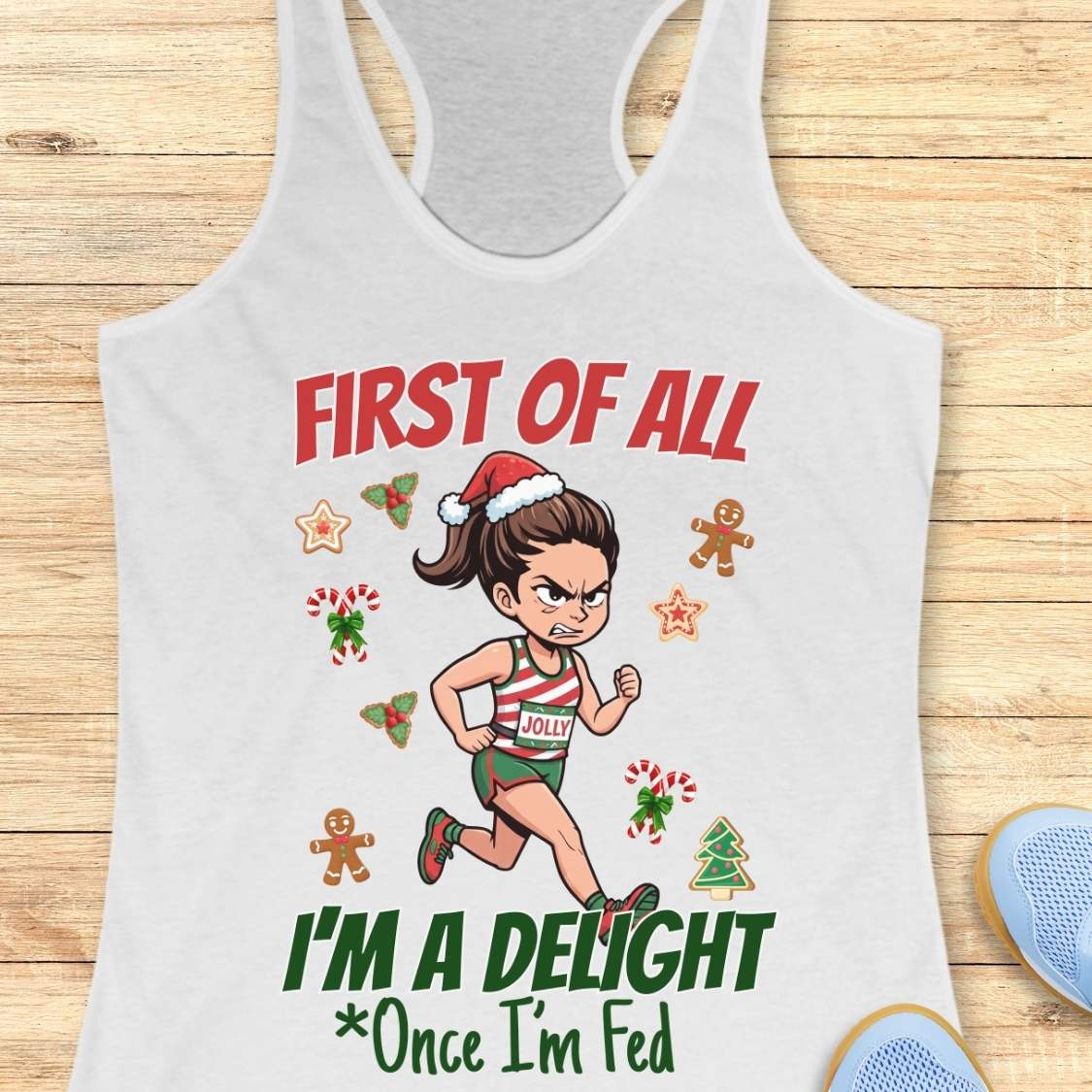 white women's racerback tank top featuring a cartoon holiday runner in a striped red, green, and white running outfit with a Santa hat. The runner is surrounded by festive Christmas elements including candy canes, gingerbread cookies, holly, star cookies, and a Christmas tree. The design reads: “FIRST OF ALL” above the runner and “I’M A DELIGHT Once I’m Fed” below. The artwork combines holiday humor with running culture in a playful, festive style.