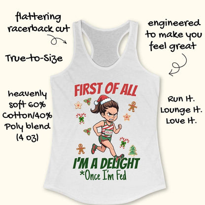 white women's racerback tank top featuring a cartoon holiday runner in a striped red, green, and white running outfit with a Santa hat. The runner is surrounded by festive Christmas elements including candy canes, gingerbread cookies, holly, star cookies, and a Christmas tree. The design reads: “FIRST OF ALL” above the runner and “I’M A DELIGHT Once I’m Fed” below. The artwork combines holiday humor with running culture in a playful, festive style.