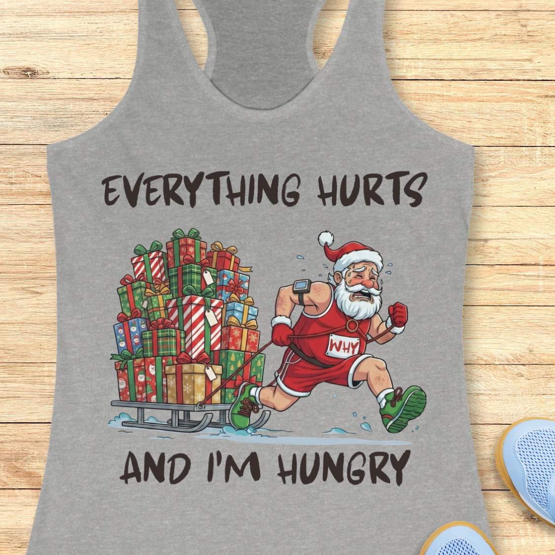 Funny Christmas running design on a grey tank top featuring a cartoon Santa Claus running while pulling a sled piled high with wrapped Christmas presents. Bold black text above and below the illustration reads: "EVERYTHING HURTS AND I'M HUNGRY." The festive artwork combines holiday humor with running and fitness themes.