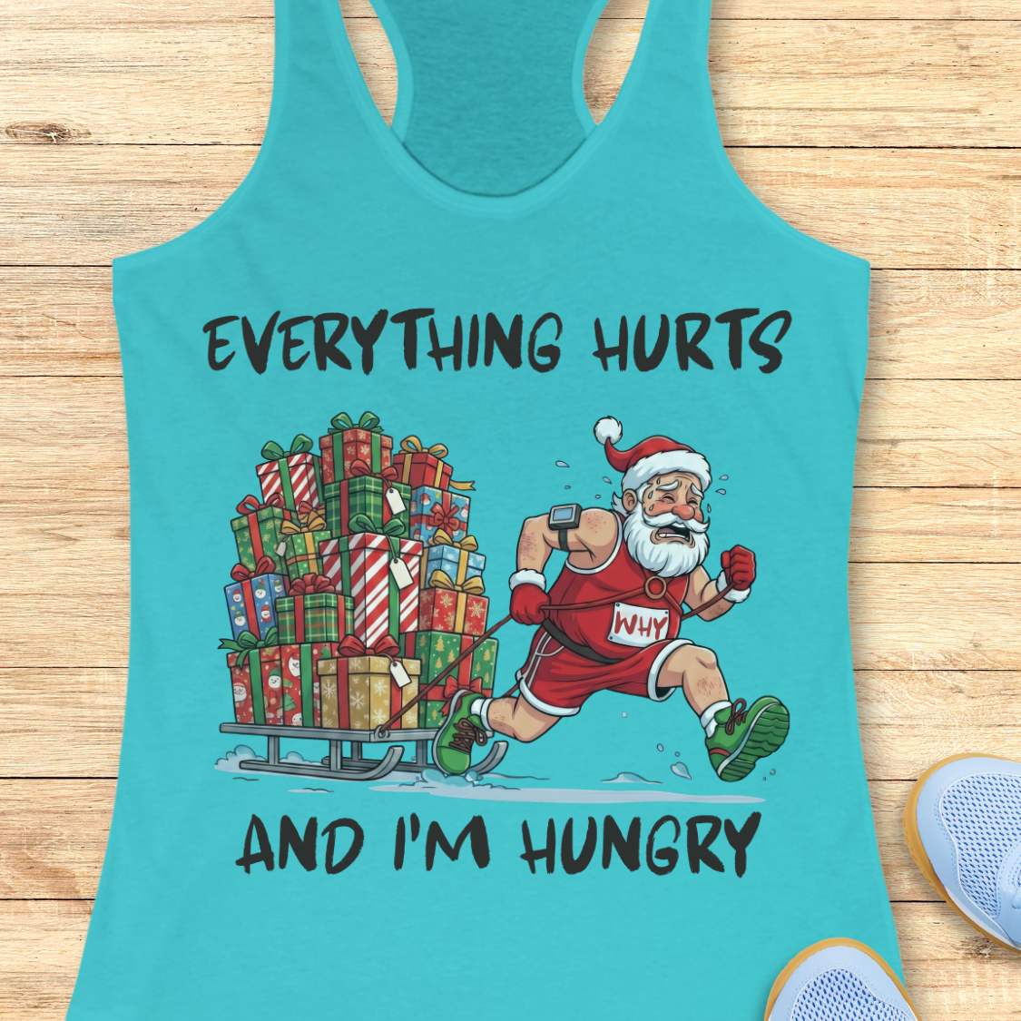 A turquoise racerback tank top laid flat on a light wood surface, featuring a graphic of Santa Claus running while pulling a sled loaded with wrapped Christmas presents. The text reads 'EVERYTHING HURTS AND I'M HUNGRY' in black lettering.