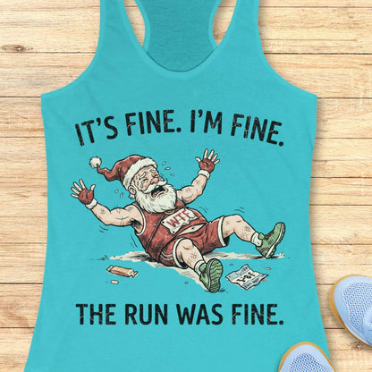 A turquoise racerback tank top laid flat on a light wood surface, featuring a cartoon of a exhausted Santa running with the text 'IT'S FINE. I'M FINE.