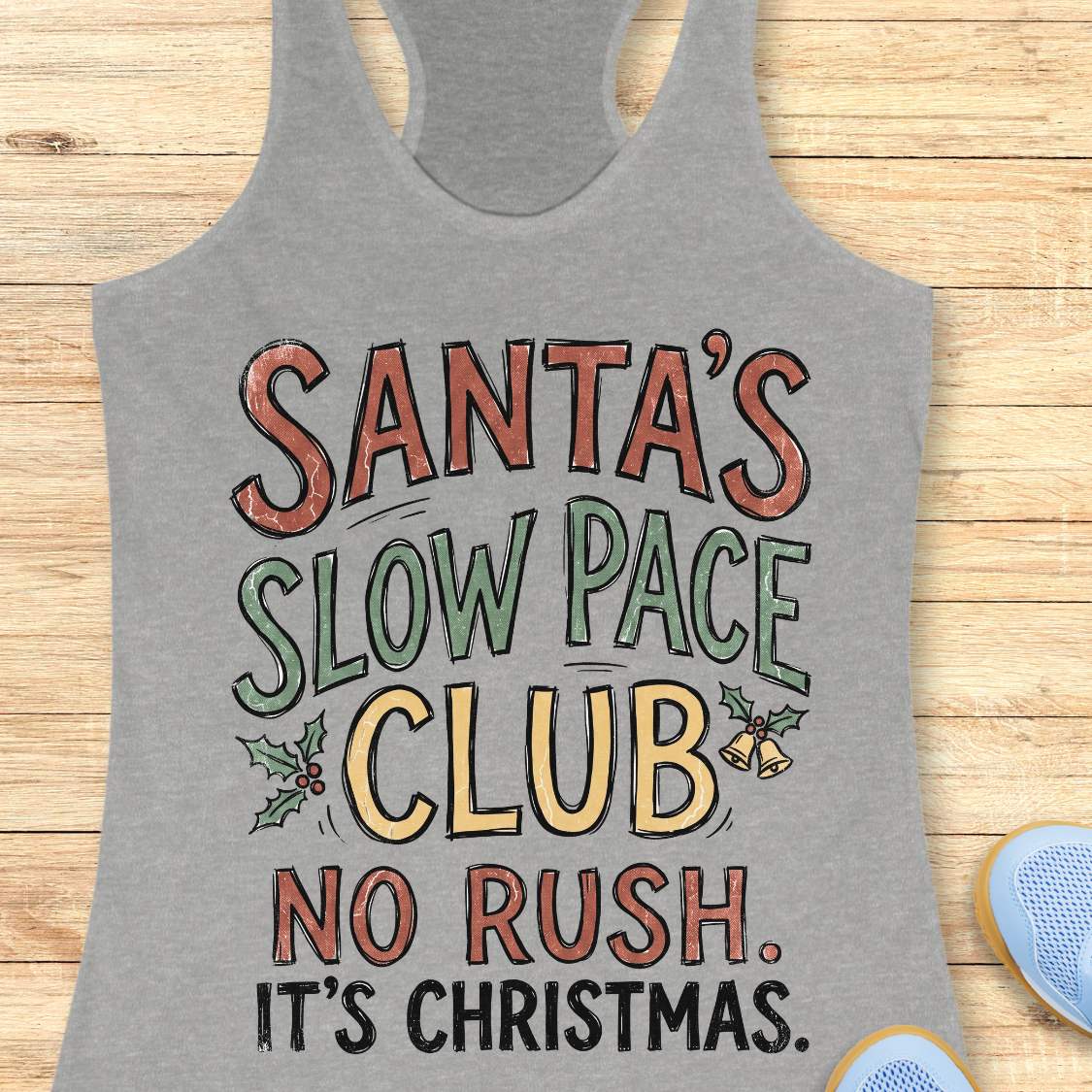 A heather gray racerback tank top with a colorful graphic text that reads 'Santa's Slow Pace Club No Rush. It's Christmas.