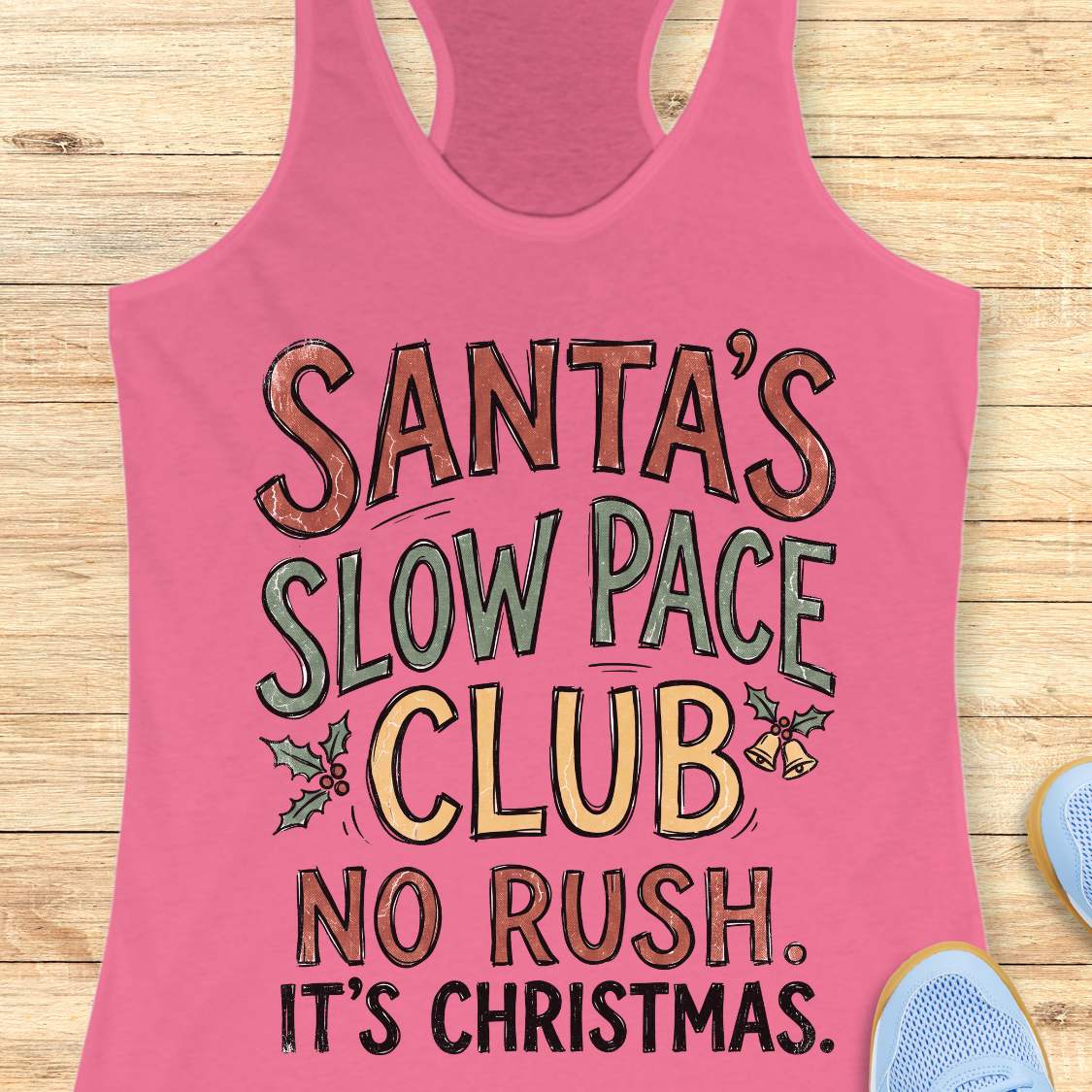 A pink racerback tank top with a festive graphic reading 'SANTA'S SLOW PACE CLUB NO RUSH. IT'S CHRISTMAS.