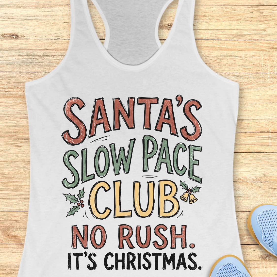A white racerback tank top with a colorful graphic that reads 'SANTA'S SLOW PACE CLUB NO RUSH. IT'S CHRISTMAS.