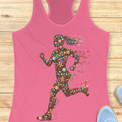 pink racerback tank top displayed on a light wood surface, featuring a colorful silhouette of a running figure made from festive Christmas elements, including string lights, gingerbread cookies, candy canes, snowflakes, ornaments, and holly. The runner's ponytail and limbs appear to dissolve into bright, scattered decorative pieces, creating a dynamic sense of motion. Partial views of blue athletic shoes are visible in the bottom corners of the image.