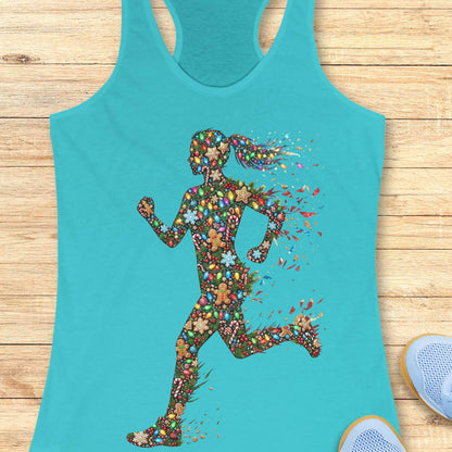 blue racerback tank top displayed on a light wood surface, featuring a colorful silhouette of a running figure made from festive Christmas elements, including string lights, gingerbread cookies, candy canes, snowflakes, ornaments, and holly. The runner's ponytail and limbs appear to dissolve into bright, scattered decorative pieces, creating a dynamic sense of motion. Partial views of blue athletic shoes are visible in the bottom corners of the image.